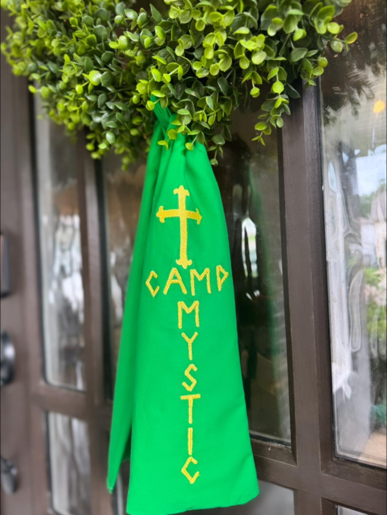 Green cape with yellow text and cross design hanging on a door